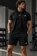 Man in de zwarte ORION Strength Set met shirt, bodywarmer en short