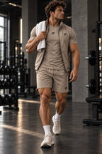 Man in de zandkleurige ORION Strength Set loopt door de gym met een handdoek