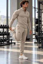 Man in de zandkleurige ORION Zip Set rekt zijn bovenbeen in de gym